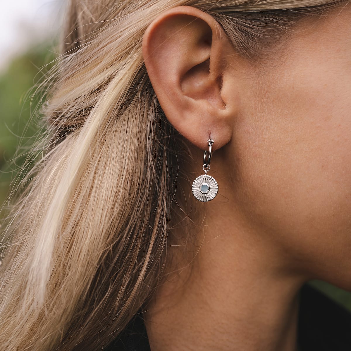 Stencil Earrings, round aquamarine and silver earrings with a modern, elegant design worn by a person.