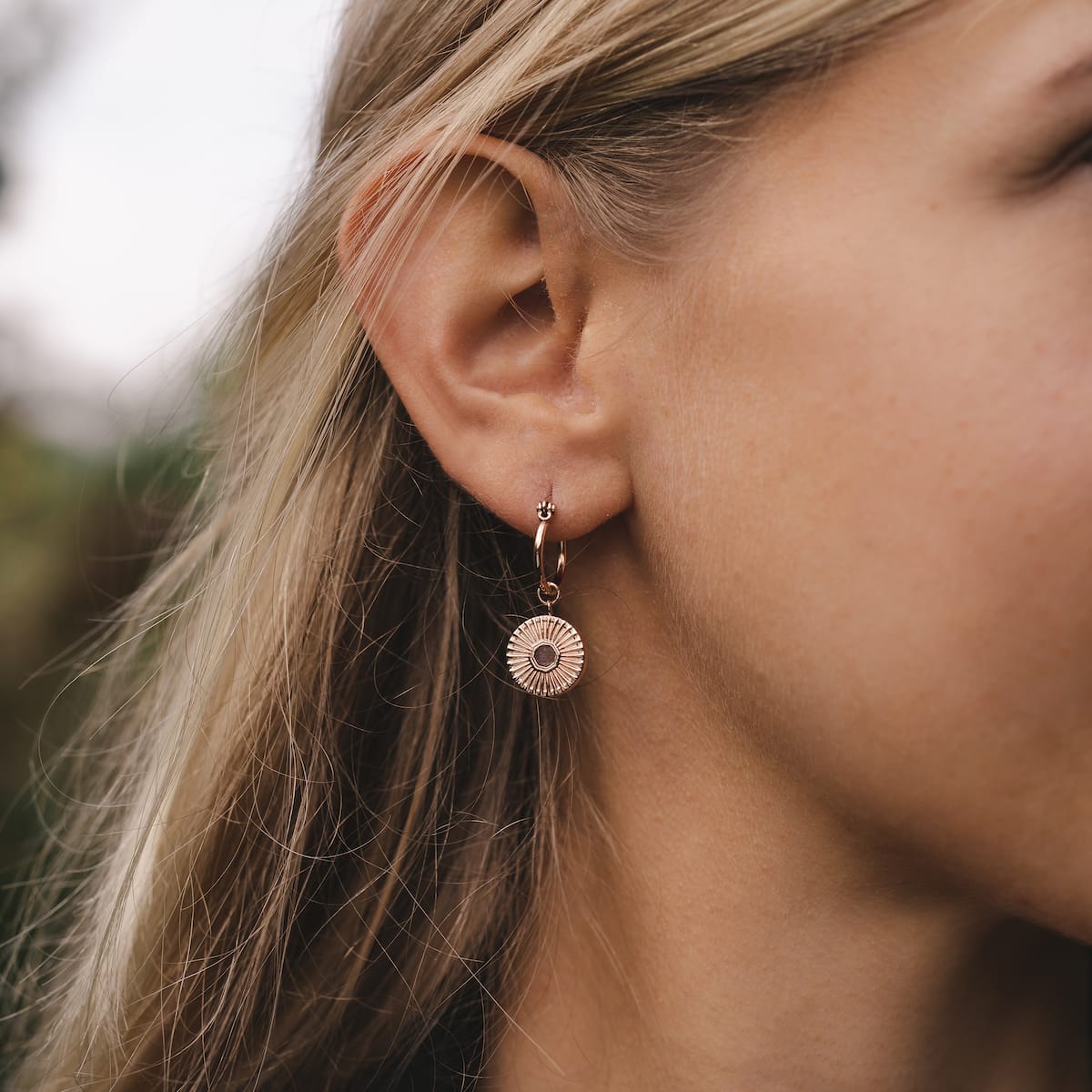 Stencil earrings, walnut and rose gold, with a delicate, circular design worn on an ear.