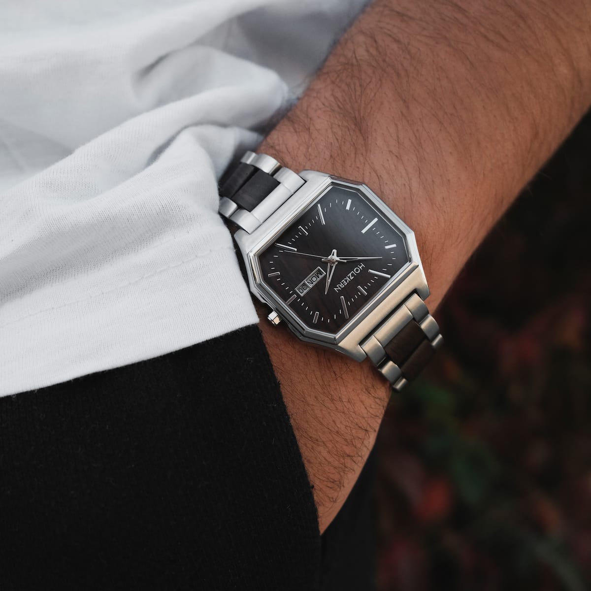 "Kéré", an elegant wristwatch with a sleek design, featuring a black dial and metal bracelet with maple accents.