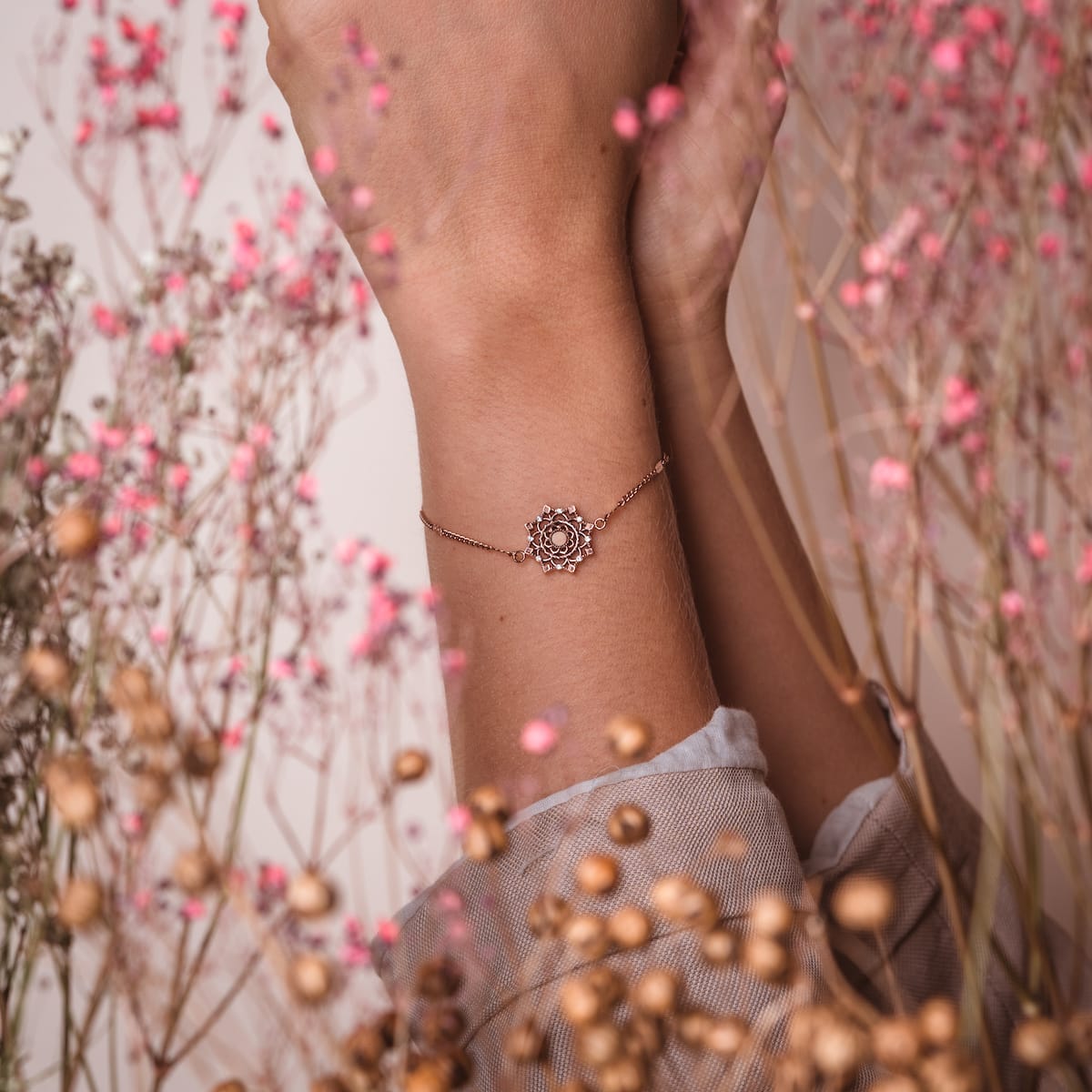 "Aphonia Bracelet", a delicate bracelet, features an intricate design in olive and rose gold hues against a natural floral backdrop.