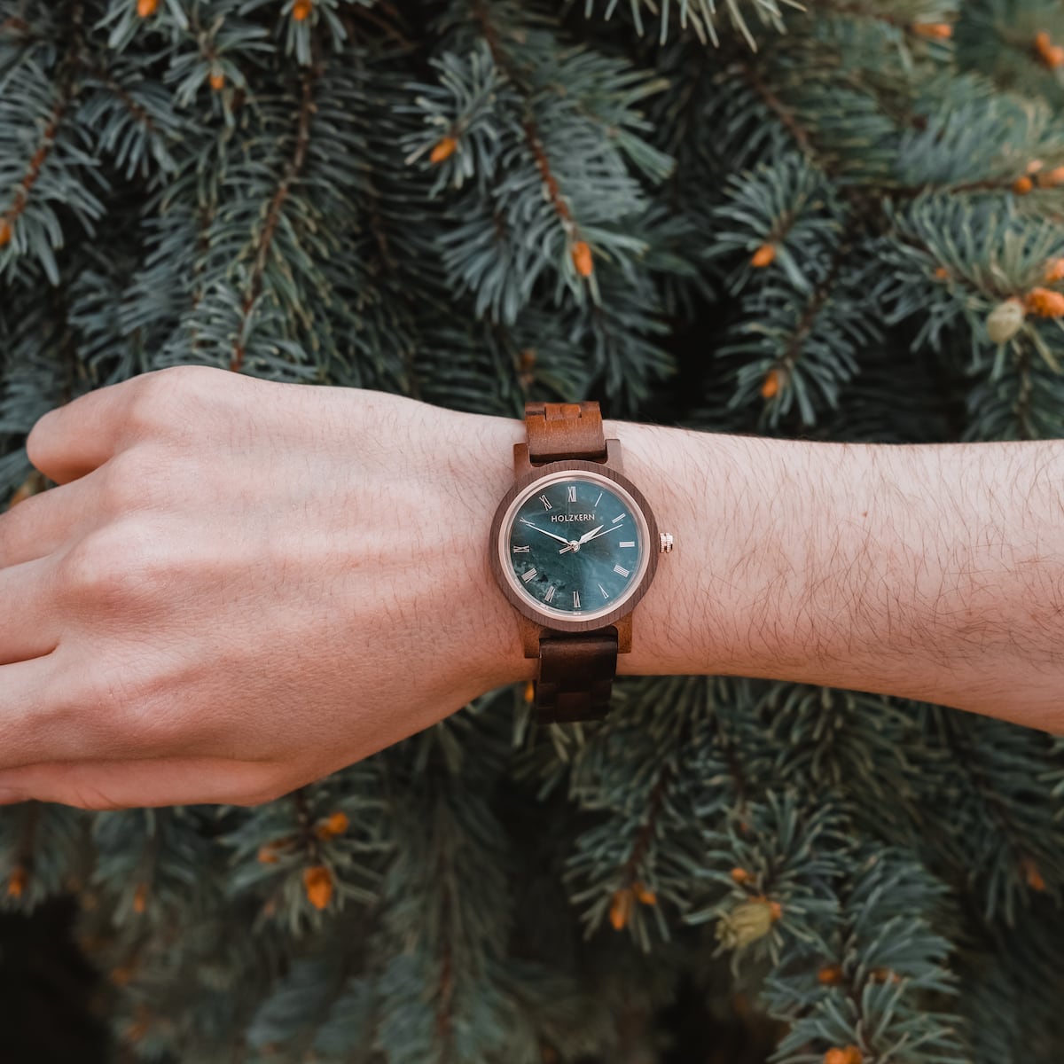 "Nymph" watch with a Walnut band and marble face, showcasing elegant natural design against a pine backdrop.