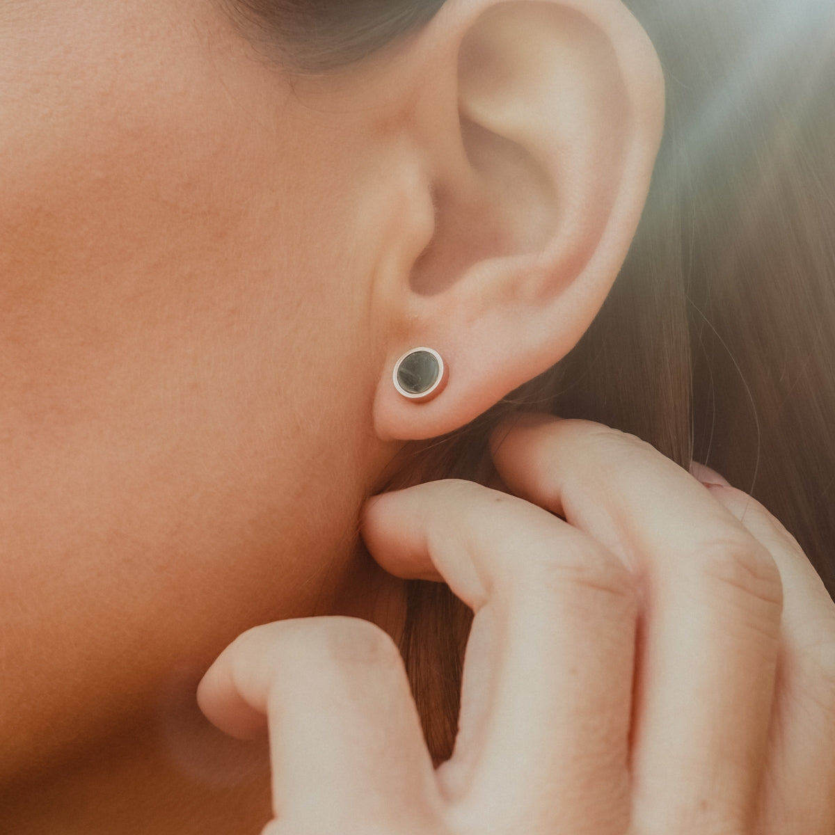 "Pigment Earrings" stud earrings with a marble and rose gold design, worn by a woman.