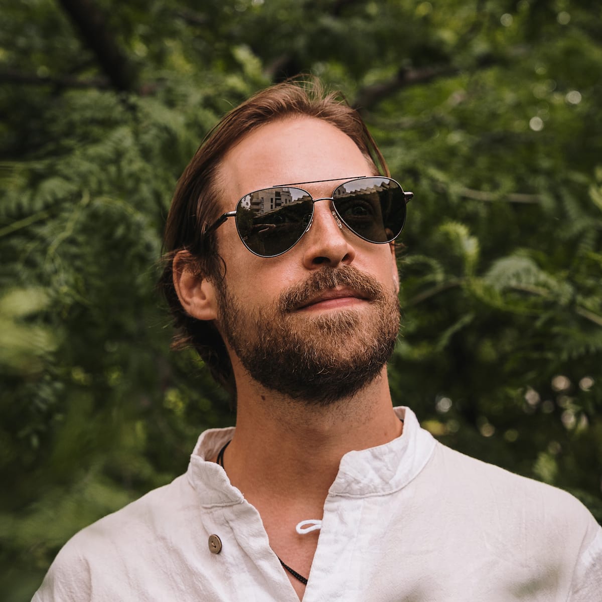 "The Badass II" sunglasses, featuring a Leadwood and Antique Silver design, worn outdoors against a lush green backdrop.