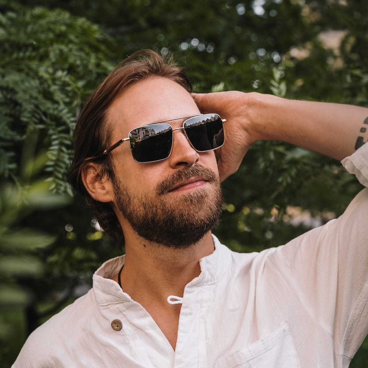 "The Talisman" sunglasses featuring a walnut and matte gold style, modeled outdoors.