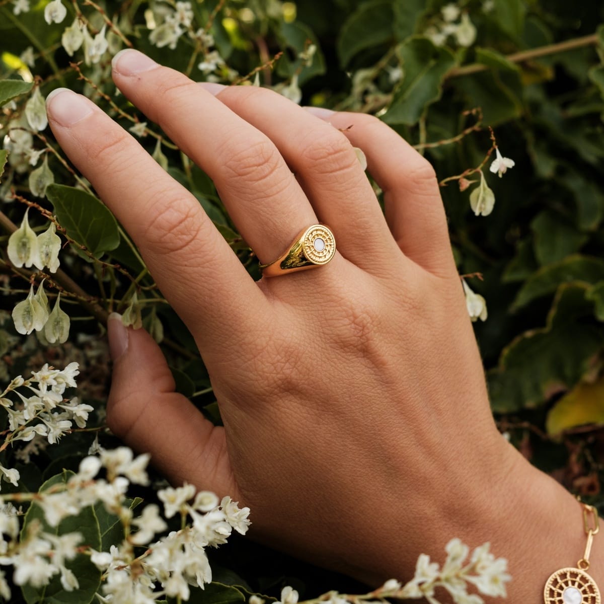 "Pixa Ring": Elegant gold ring with white nacre detail amidst lush greenery.