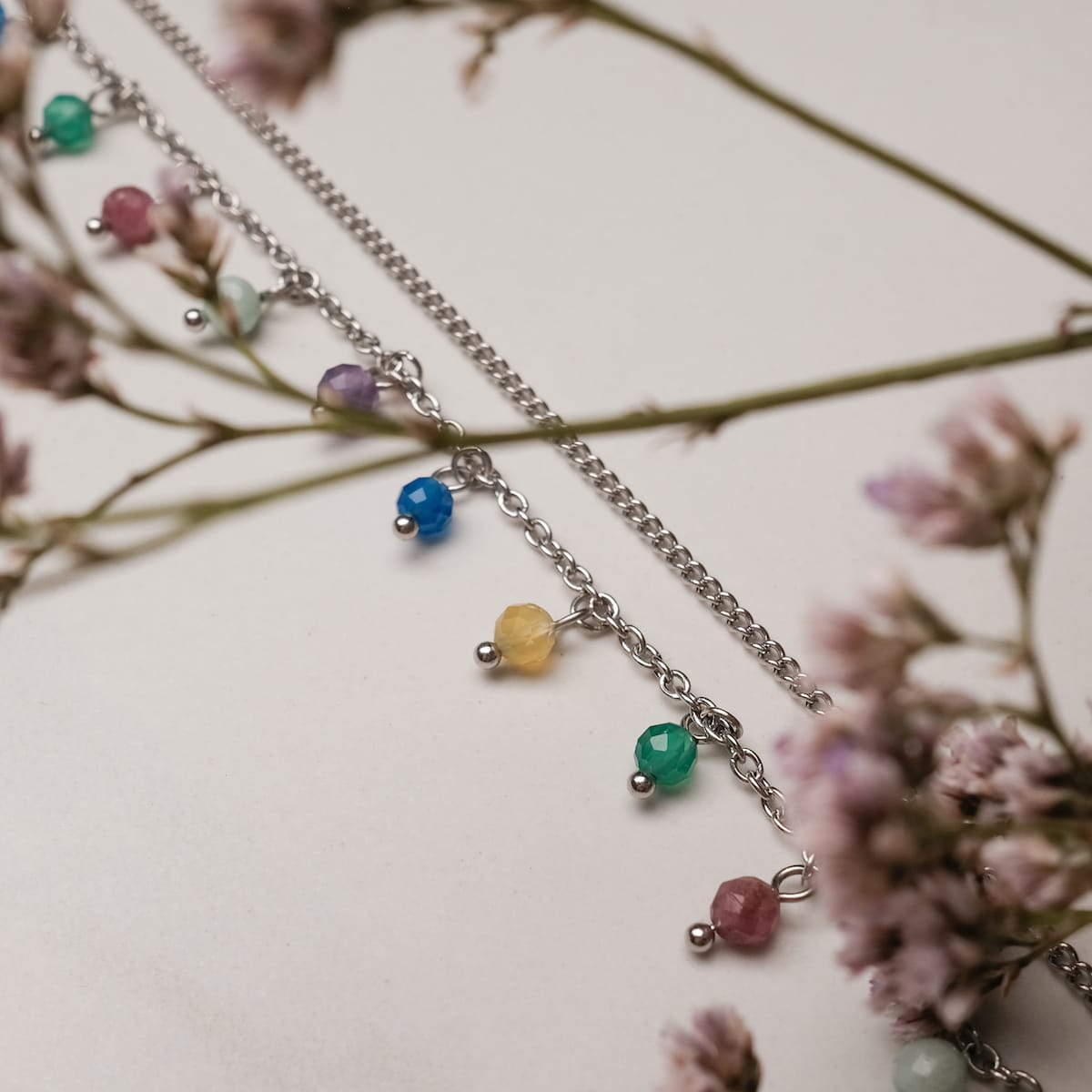 "Free Play Necklace", a necklace with a rainbow style and silver chain, elegantly showcased with floral accents.