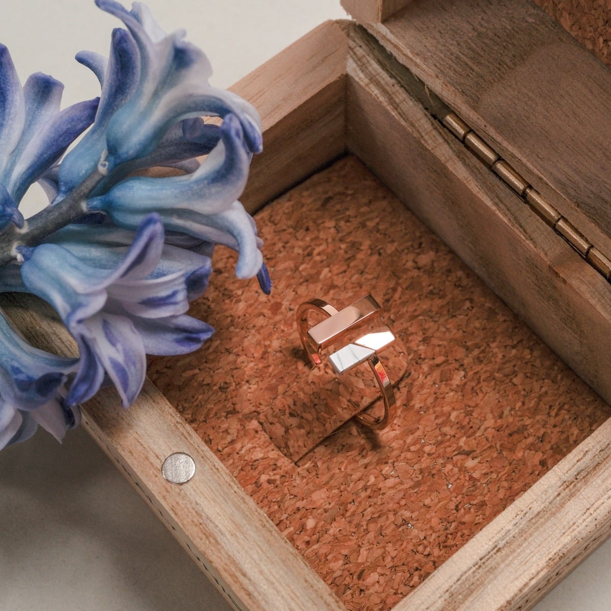 "Campania Ring", a marble and rose gold ring, displayed elegantly in a wooden box with a blue flower accent.