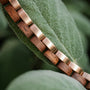 "Duet", bracelet, features a sleek walnut and rose gold design against a natural background.