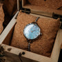 "Brighter" watch in nacre and silver finish, featuring an elegant design with a blue-toned dial, showcased in a wooden box.
