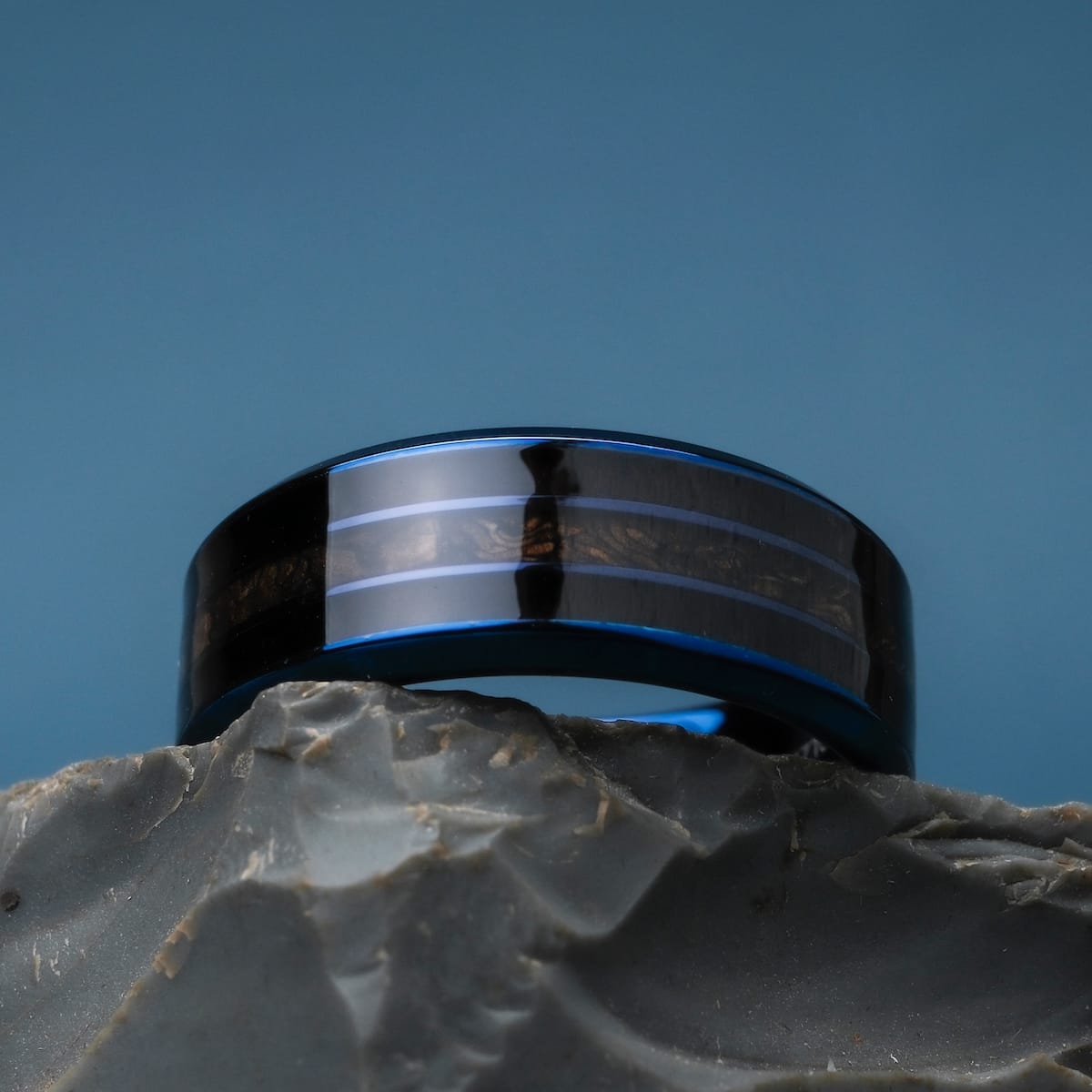 "Cartesian Ring", a stylish ring with a maple wood inlay and blue accents, showcased on a stone surface.