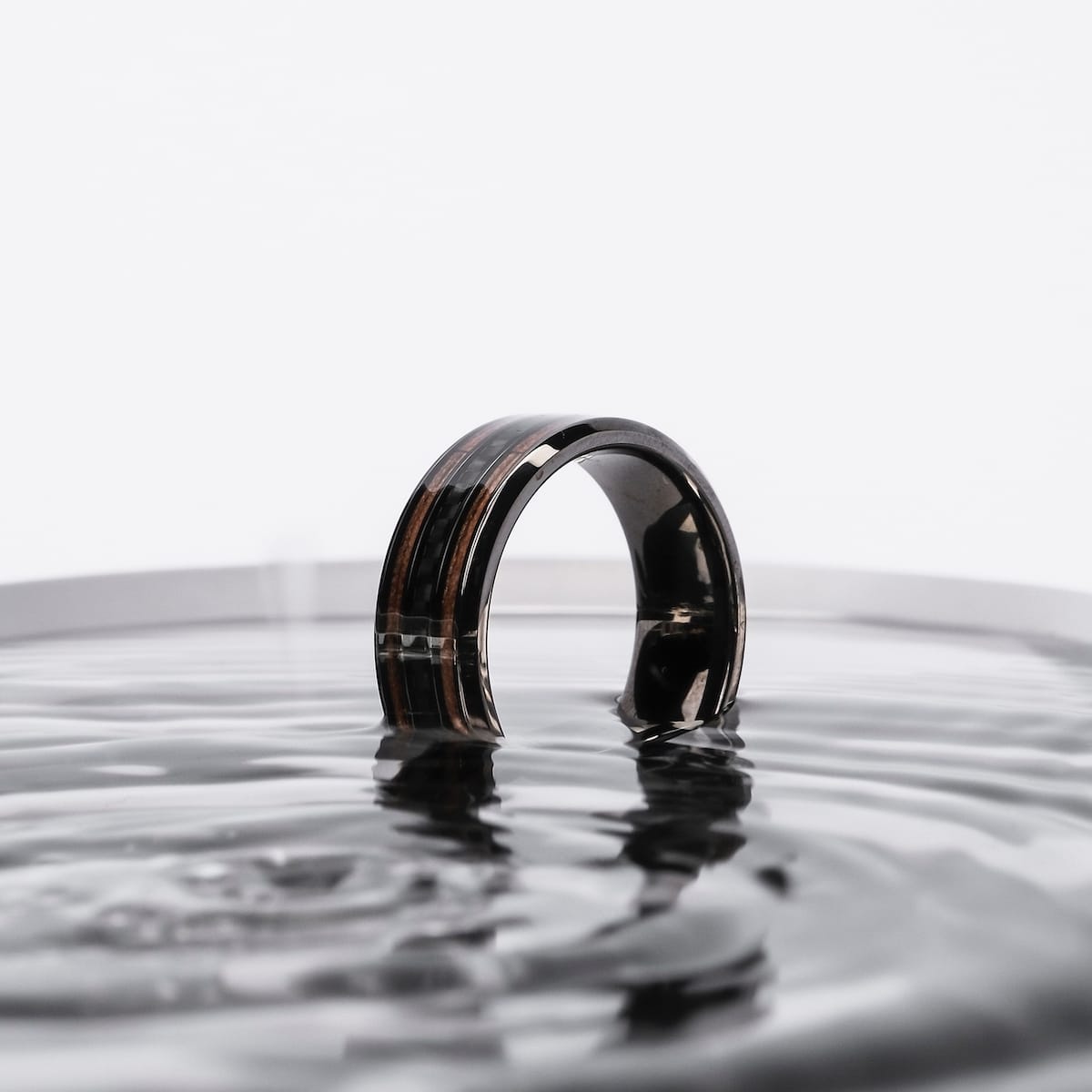 "Cartesian Ring" ring, featuring a sleek walnut and carbon design, emerging stylishly from rippling water.