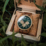 "Canopy", a stylish watch with zebrawood and marble details, displayed in a wooden box amidst greenery.