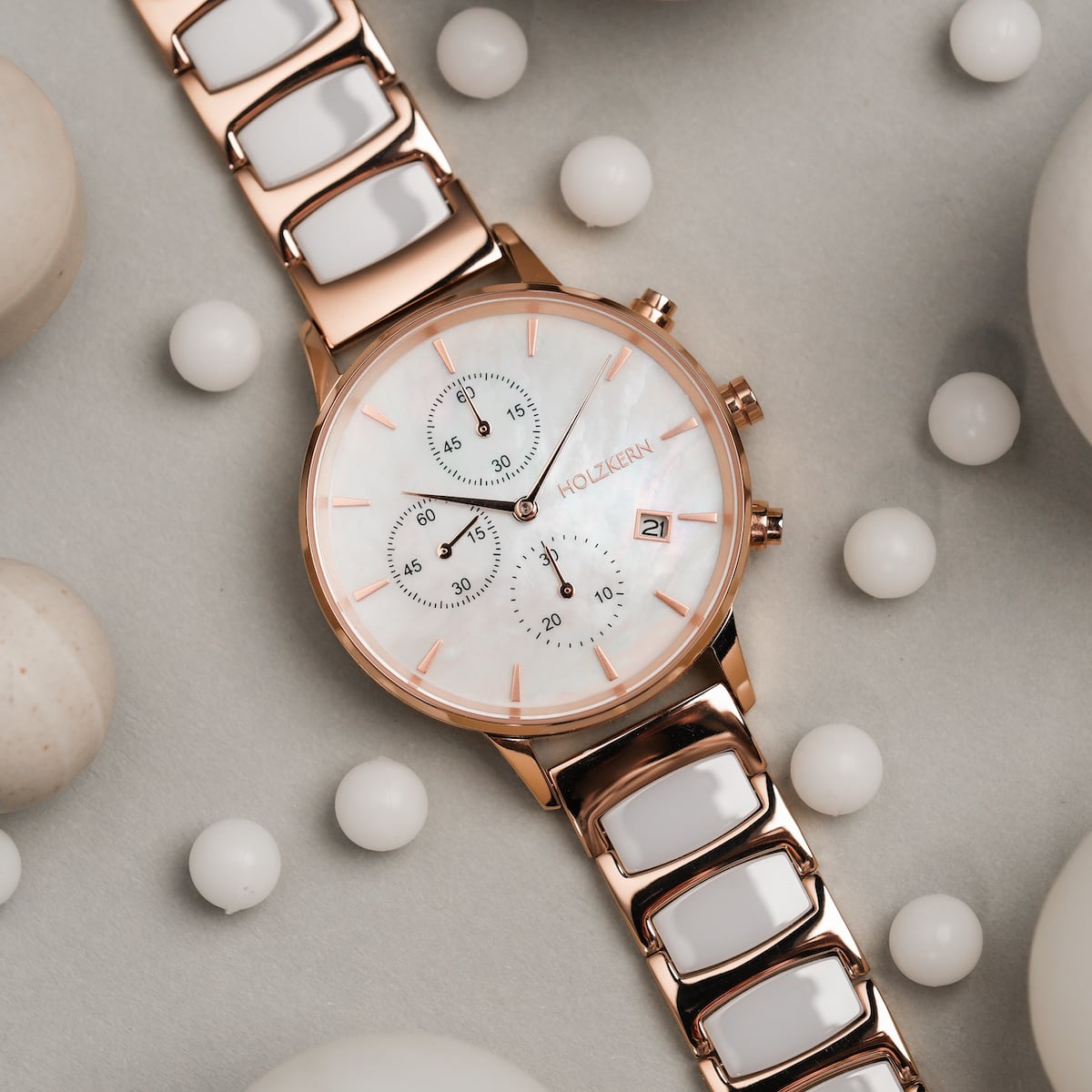 "Shiny" watch featuring nacre dial and ceramic links in a rose gold finish, surrounded by white spheres.
