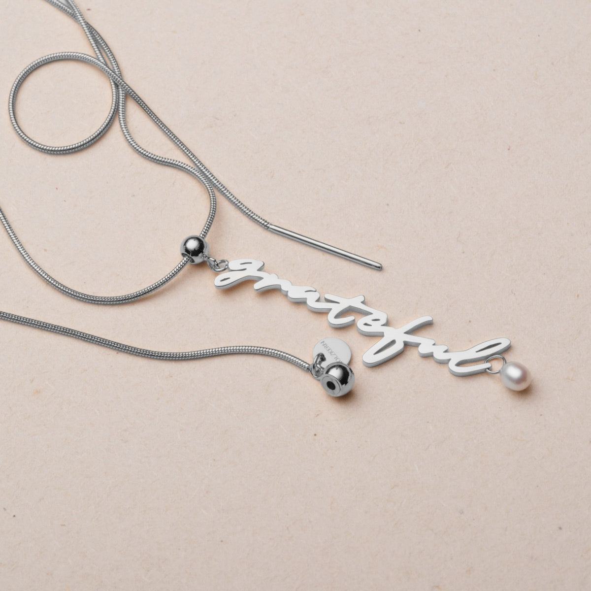 "Grateful-Charm" necklace with elegant pearls and silver, featuring a delicate charm and stylish script design.