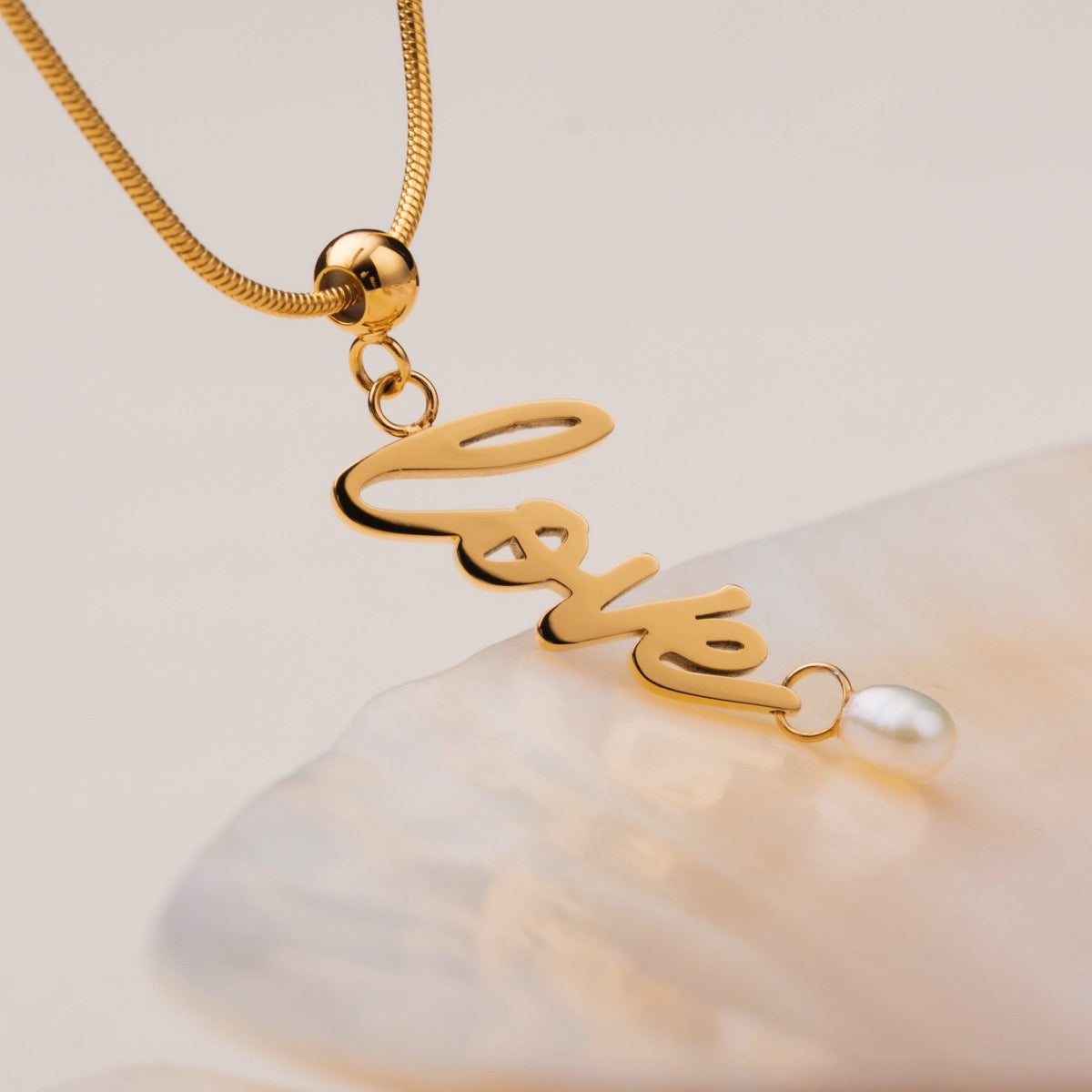 "Love-Charm" necklace features elegant gold script with a pearl accent, showcasing a charming, sophisticated design.