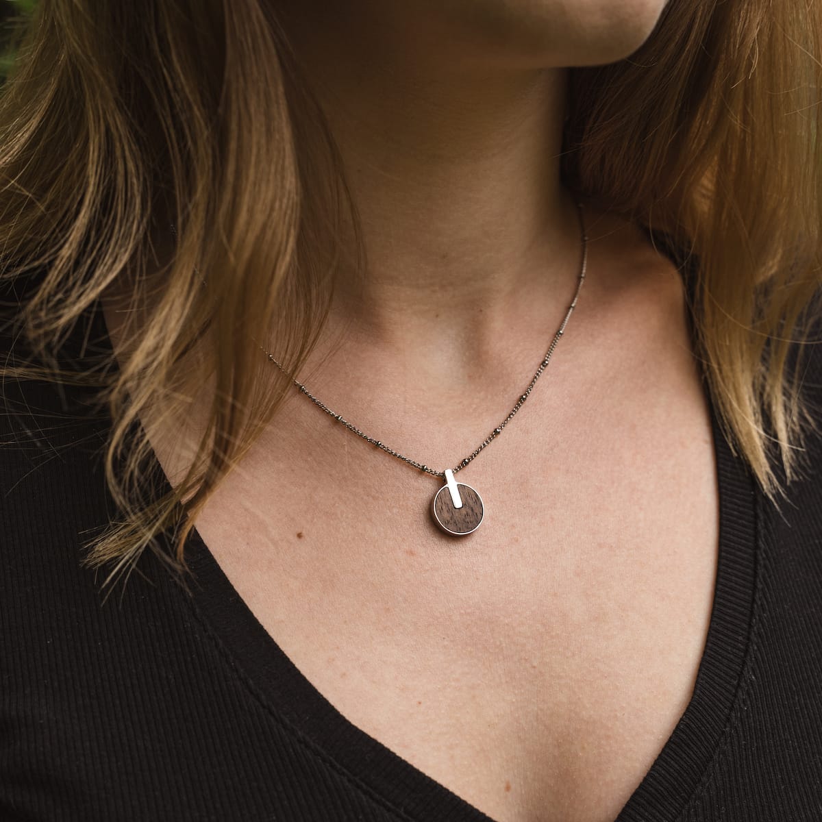 "Opacity Necklace", a stylish necklace, featuring a walnut and silver pendant on a delicate chain.