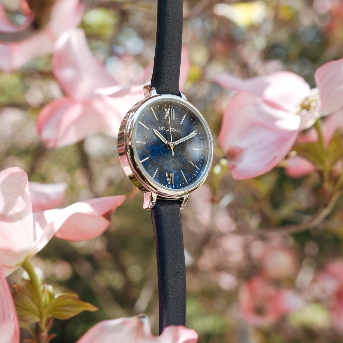 "Teresa" watch featuring a lapis lazuli face and silver accents amidst blooming flowers.