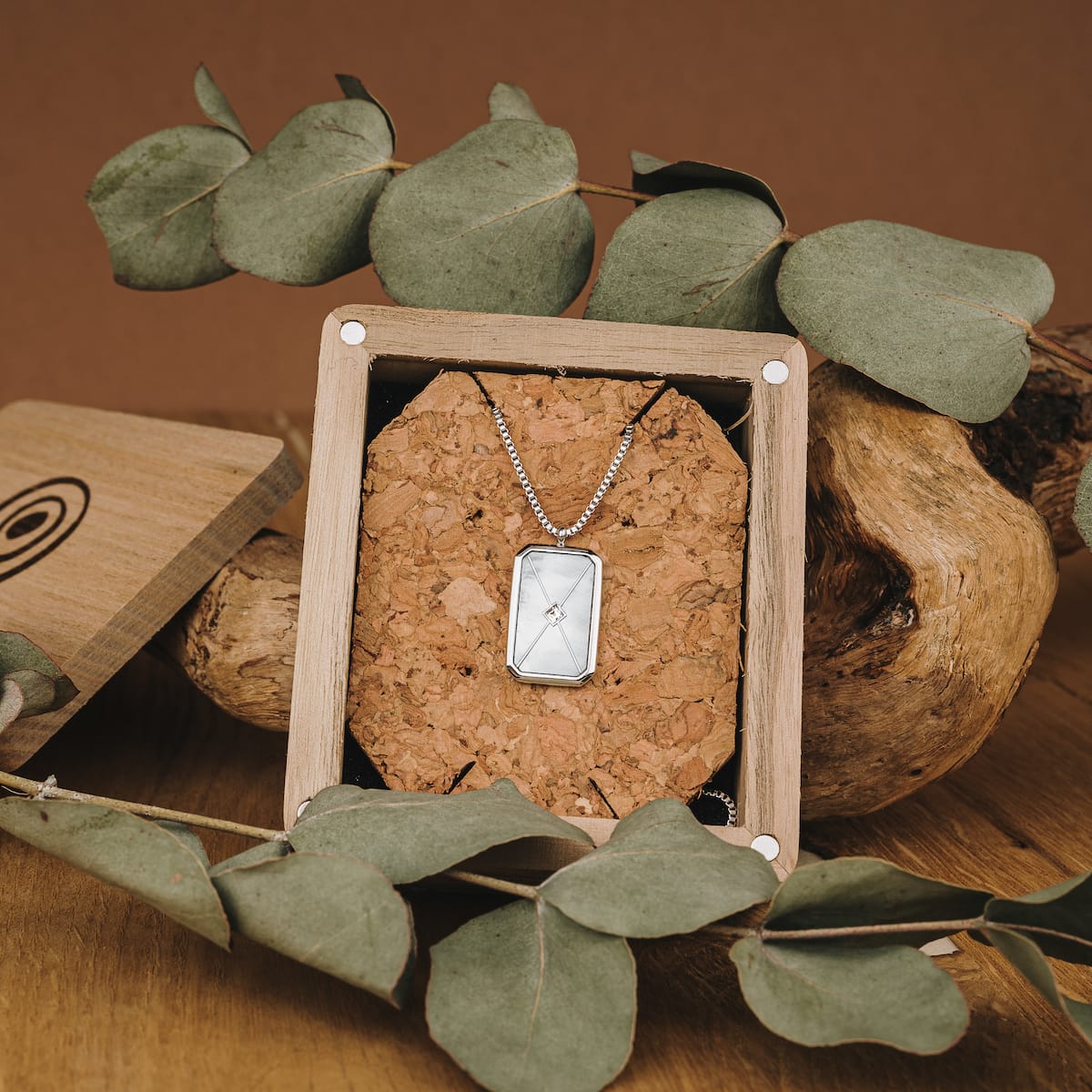 "Aquarell Necklace", an elegant necklace with a white nacre and silver design, presented in a rustic display setting.