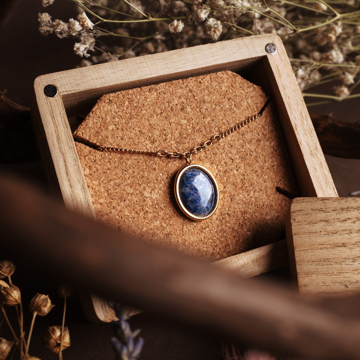 "Mirror Necklace" necklace, featuring a lapis lazuli pendant set in gold, displayed on a cork background for a rustic look.