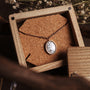 "Mirror Necklace" necklace featuring a turquoise stone set in rose gold, styled in a rustic wooden box.