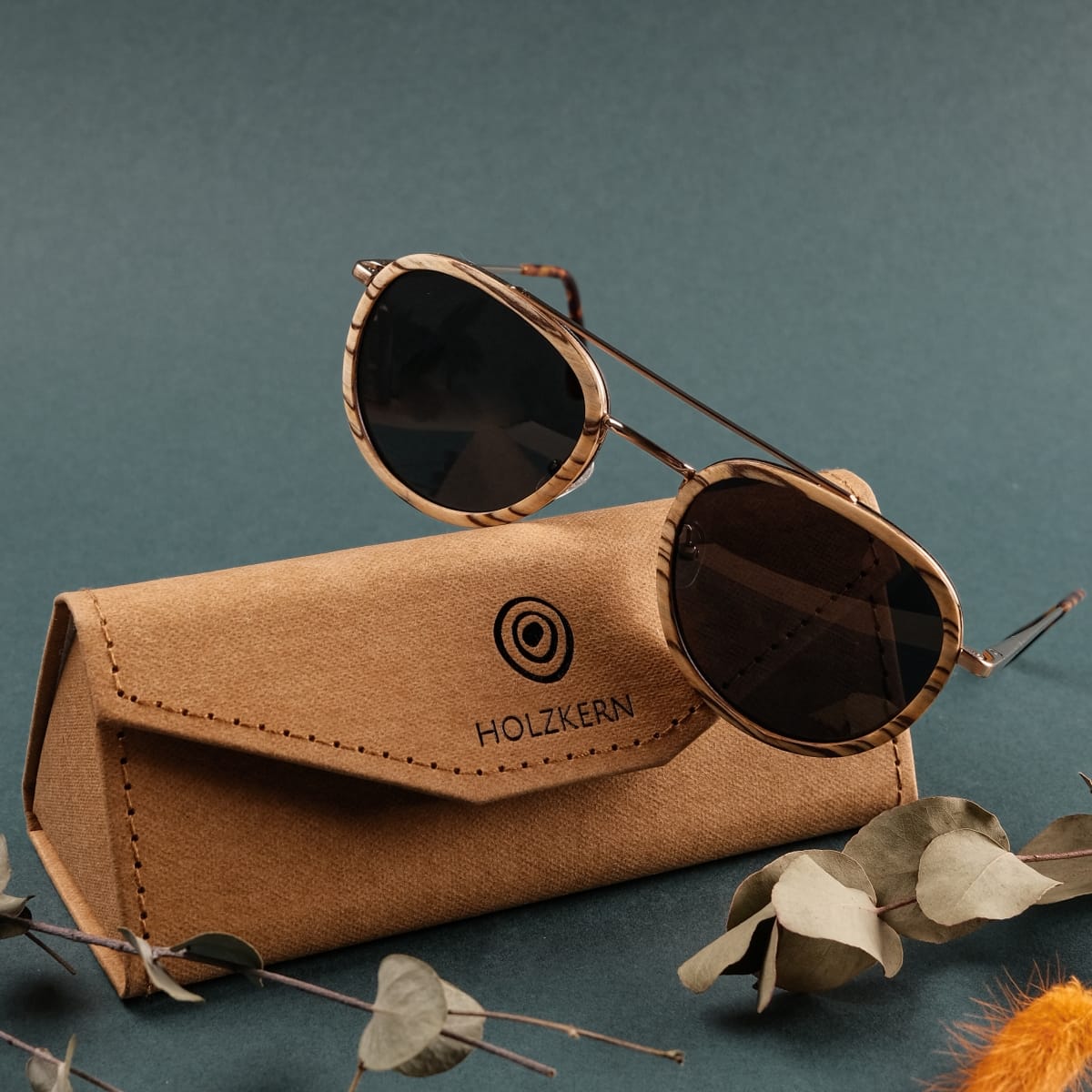 "The Risky" sunglasses with Zebrawood frames and matte gold accents, displayed with a stylish case.