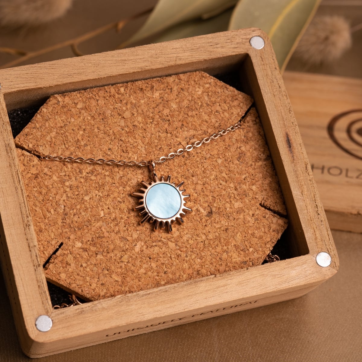 "Shade Necklace": Elegant necklace featuring a blue nacre pendant on a rose gold chain, displayed in a wooden box.