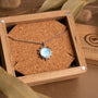 "Shade Necklace" necklace featuring a blue nacre center in a silver sunburst design, presented in a wooden box.