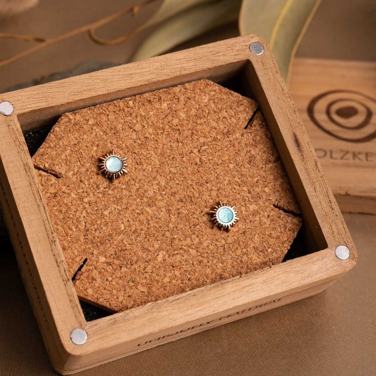 "Shade Earrings": Rose gold earrings with blue nacre, elegantly displayed in a wooden box.