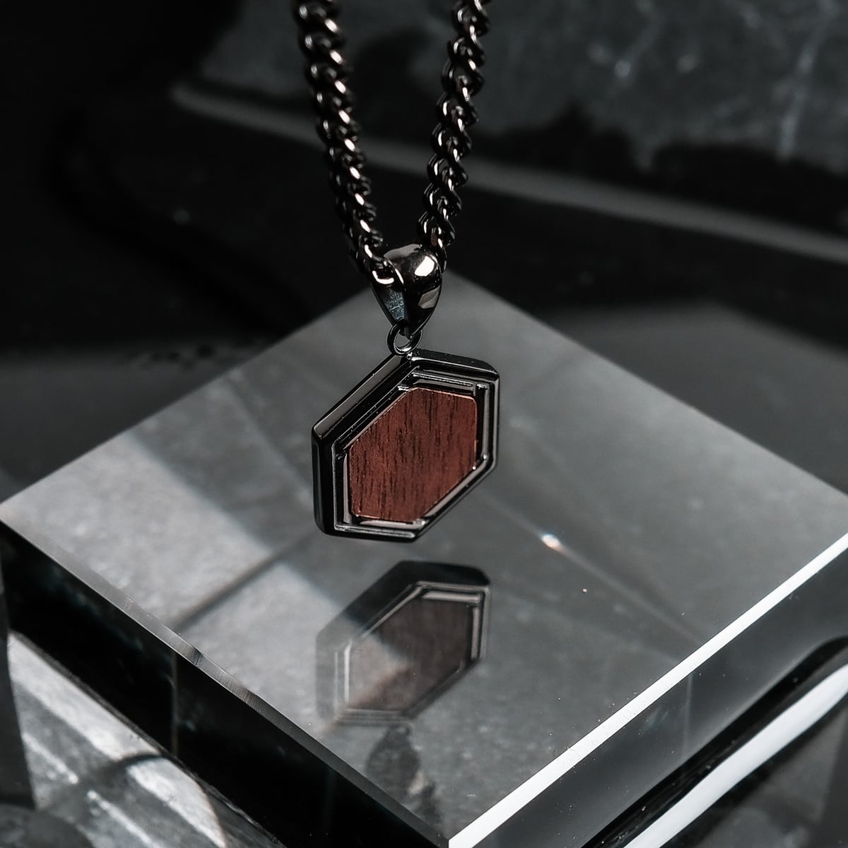 "Axis Necklace", a necklace featuring a hexagonal pendant with a walnut wood insert and dark gray metal frame.