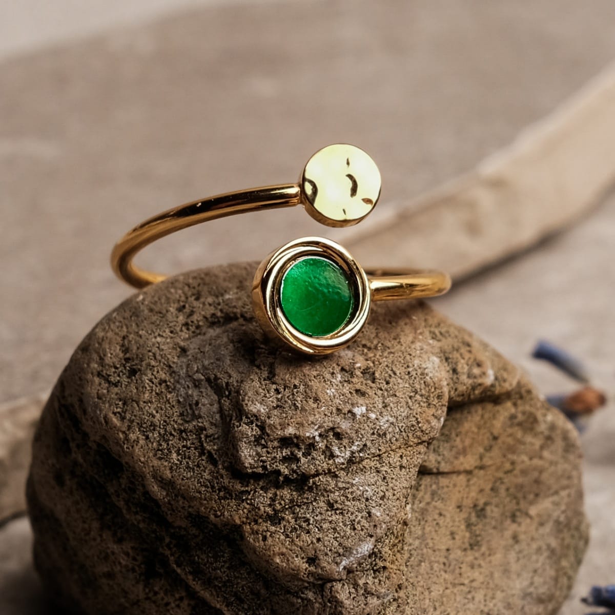 "Zendala Ring" ring featuring green nacre and gold, set on a rustic stone backdrop, showcasing its elegant open design.