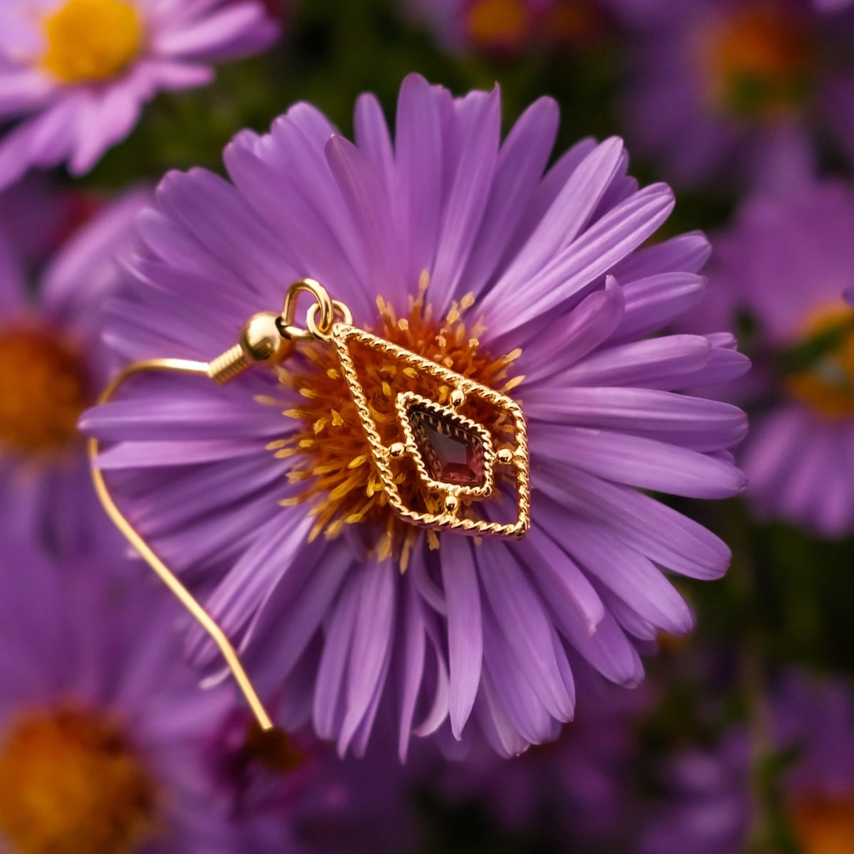 Daydreamer earrings, elegant gold earrings with amethyst centerpiece, displayed against vibrant purple petals.