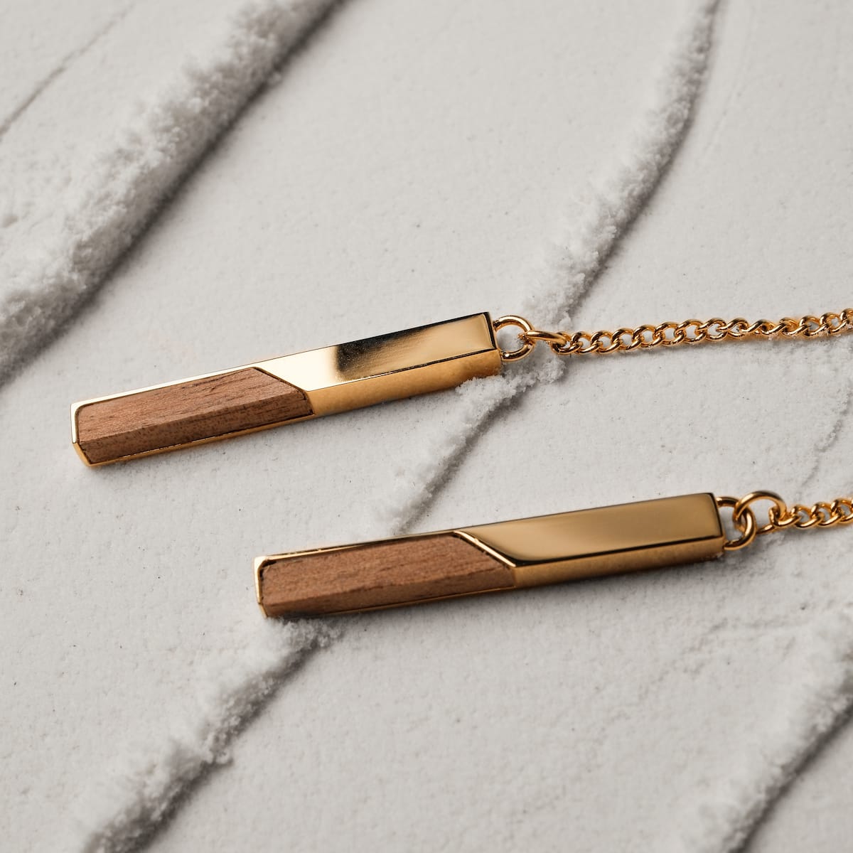 "Campania Earrings" earrings featuring a sleek design with koa wood and gold accents on a textured background.