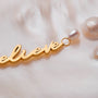 "Believe-Charm", a charm featuring gold script and pearls, showcasing elegance and sophistication.