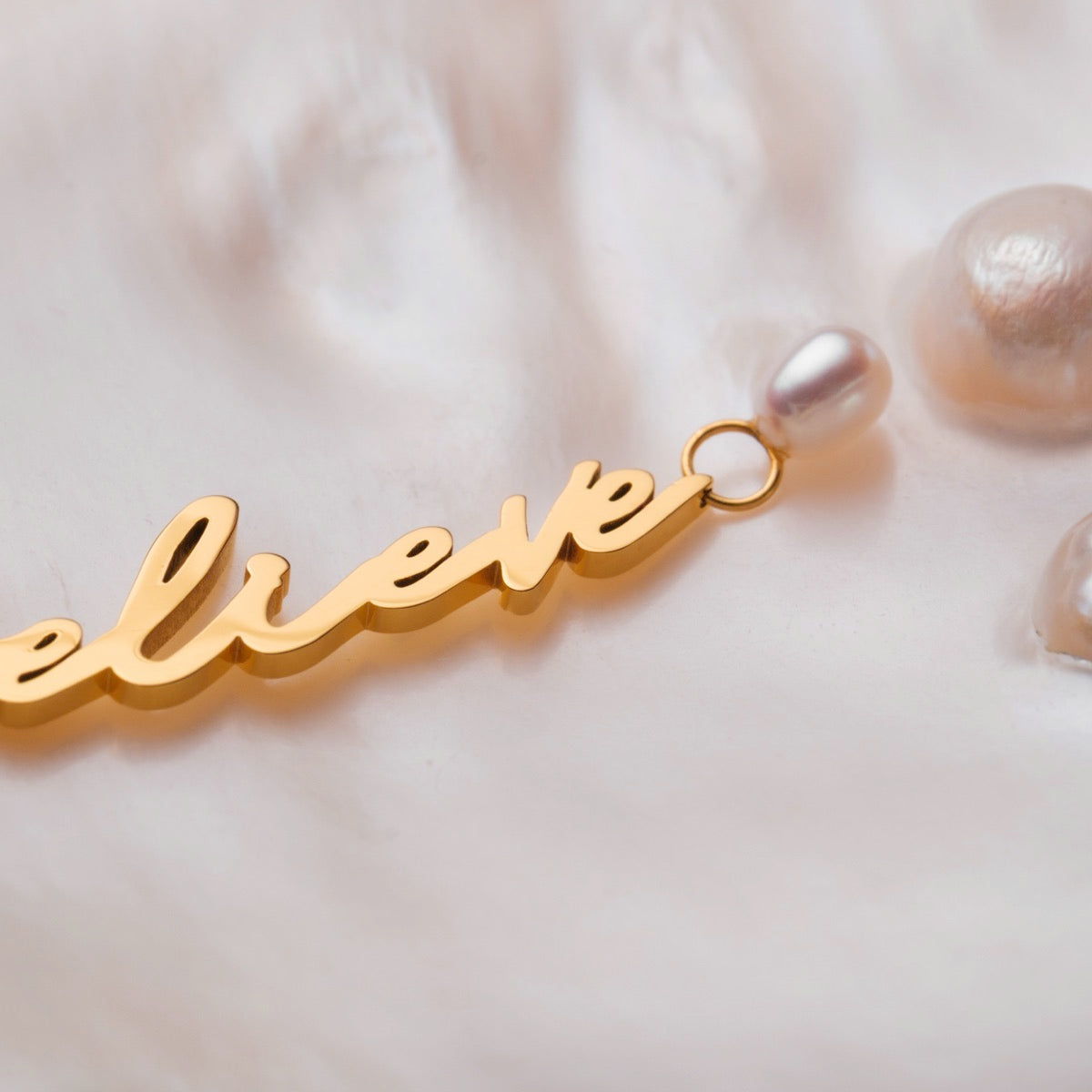 "Believe-Charm", a charm featuring gold script and pearls, showcasing elegance and sophistication.