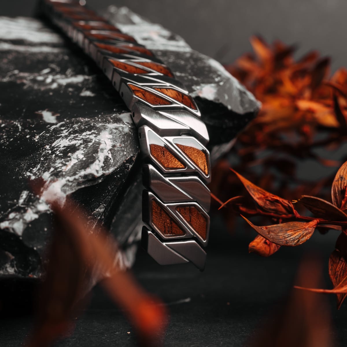 "Baritone", a stylish bracelet with walnut inlay and silver accents, showcased on a dark, textured background with autumn foliage.