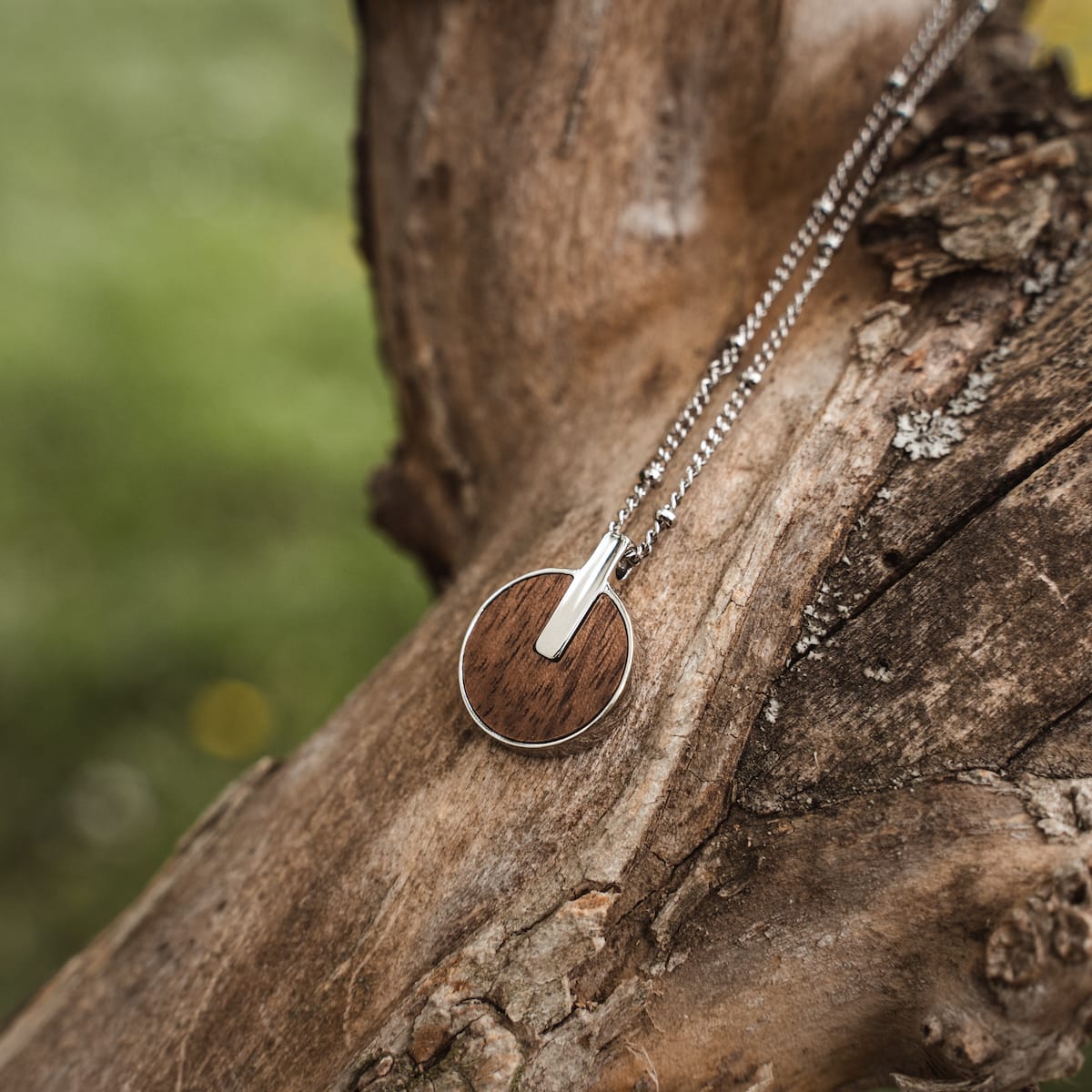 "Opacity Necklace", a stylish necklace in walnut and silver, displayed on rustic wood.