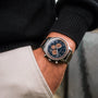 "Oscar" watch featuring a Walnut finish and blue dial, worn by a person in casual attire.