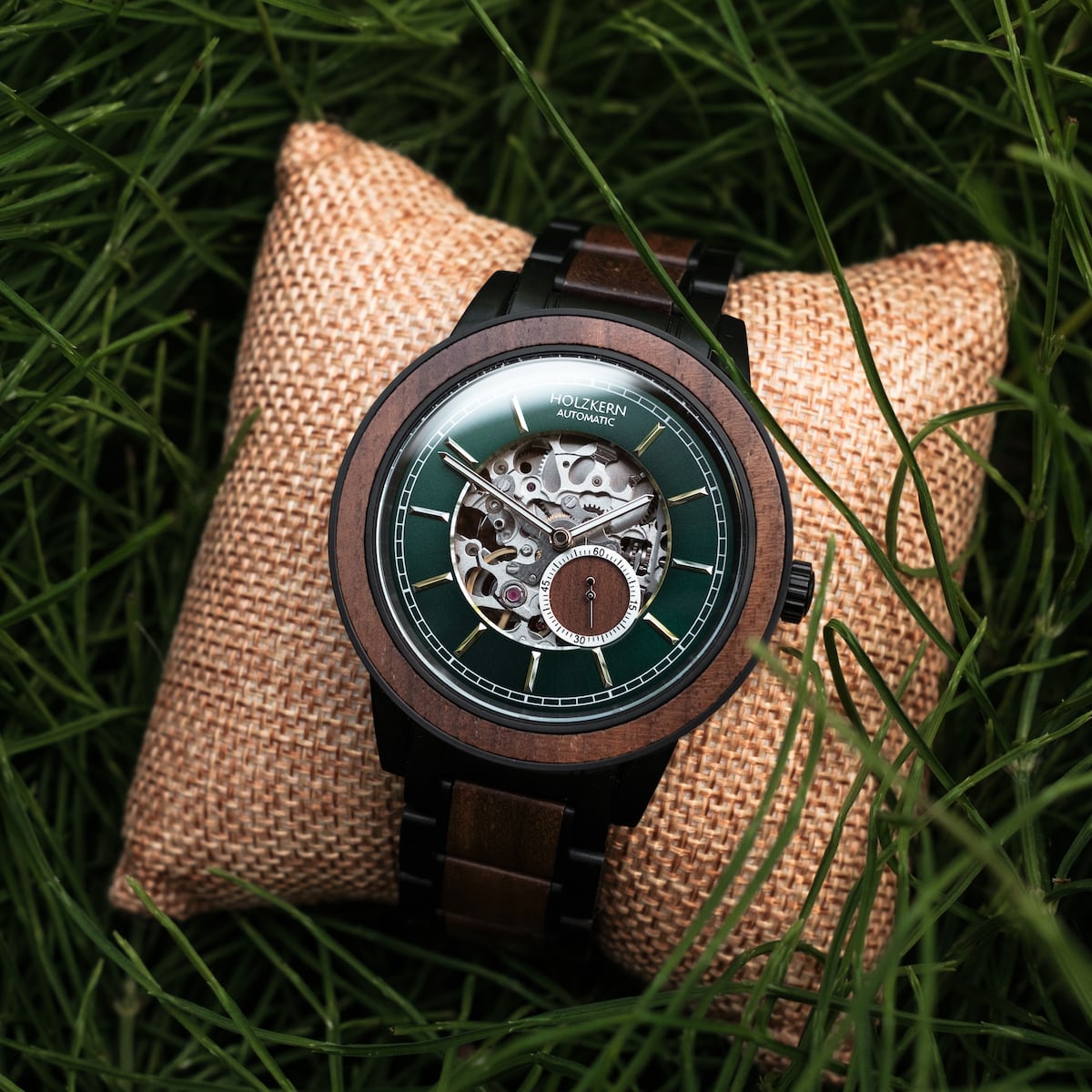 "Sigiriya" watch, featuring a walnut design with a green dial set on a rustic cushion surrounded by grass.