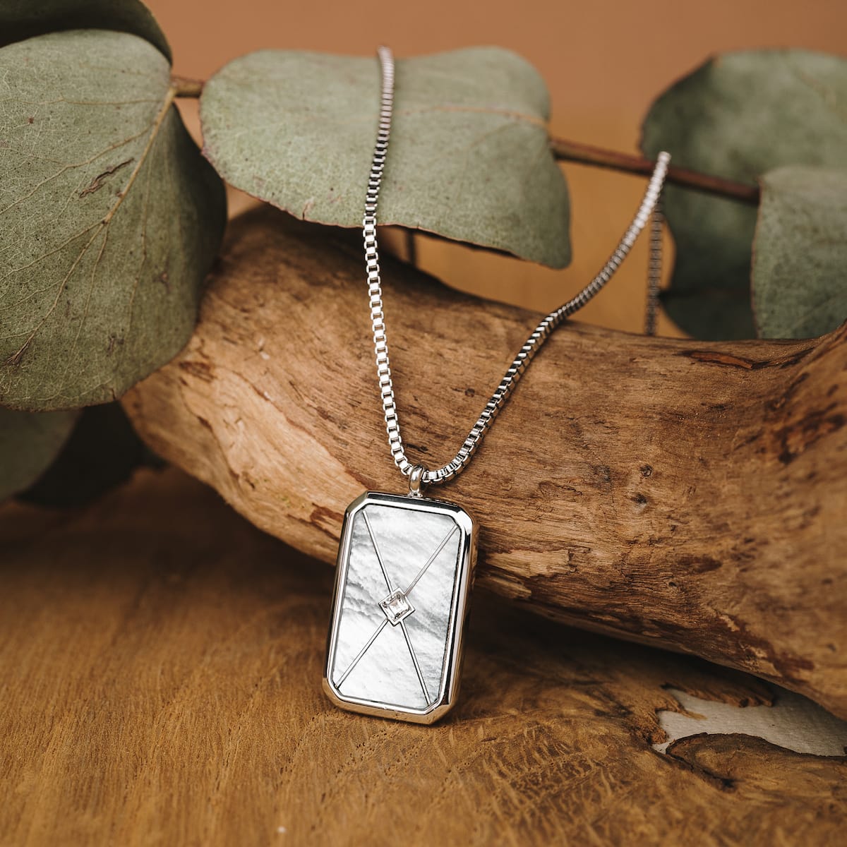 "Aquarell Necklace", a stylish silver necklace featuring a white nacre pendant, elegantly displayed against a natural wooden background.