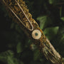 "Stencil Necklace", a stylish necklace featuring a marble center and gold accents, displayed against a natural background.