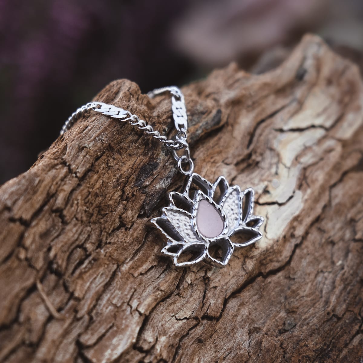 "Balance Necklace", a silver lotus-shaped necklace with a marble accent, resting on rustic wood.
