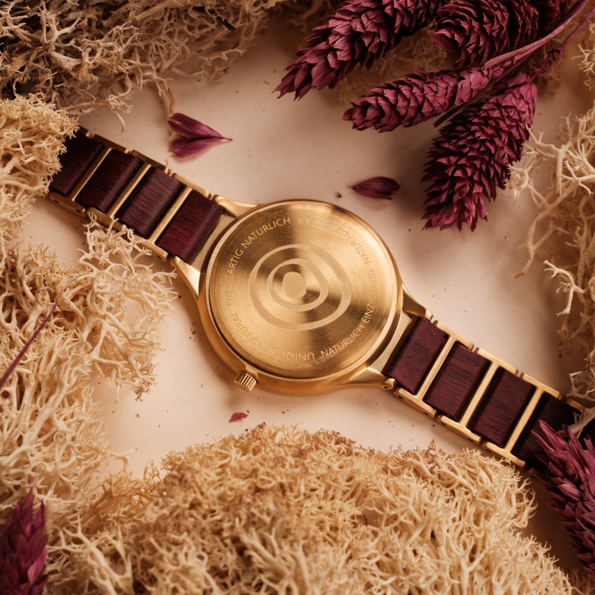 "Mauritius" watch featuring a gold-tone backplate and amaranth accents, styled with elegant natural elements.