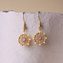 "Aphonia Earrings" earrings with amethyst center and intricate gold design on a textured background.