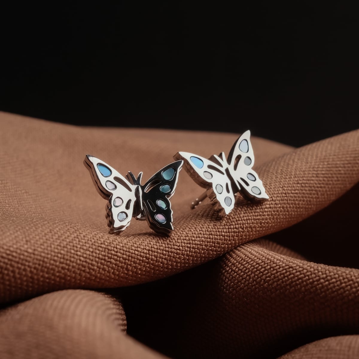 "Fritillary earrings" butterfly earrings in nacre and silver, featuring a delicate, iridescent design on a soft brown fabric background.