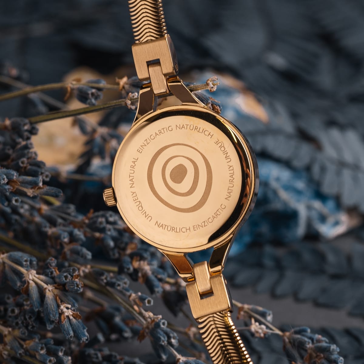 "Shesha", a gold watch with a sleek, sophisticated design highlighted by nacre detailing against a natural backdrop.