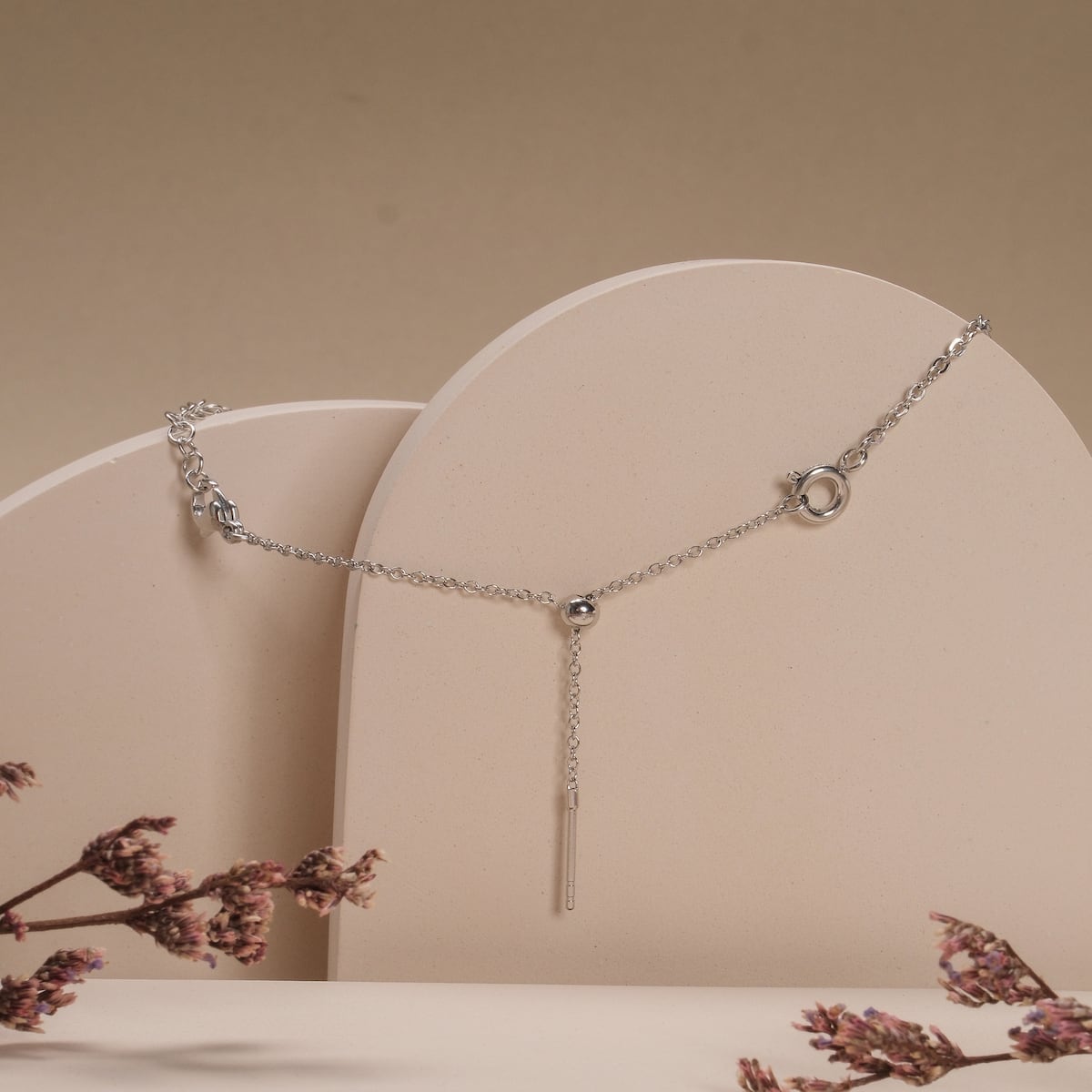 "Jewelry Extender" silver jewelry extender on minimalist beige backdrop with decorative flowers.