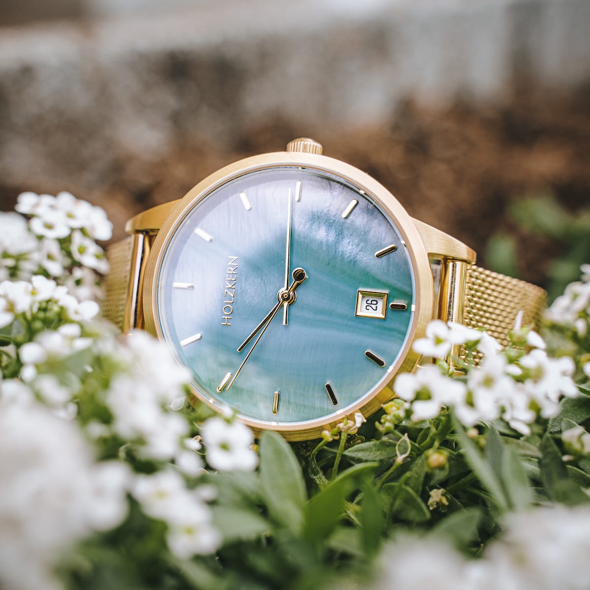 "Talamanca" elegant watch with nacre face and gold accents, styled with delicate floral surroundings.