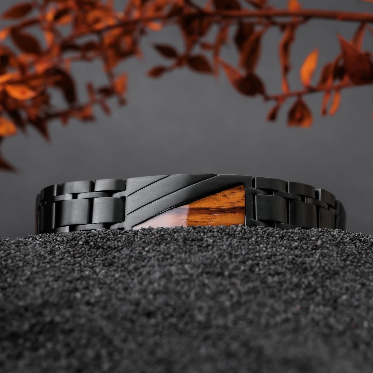 "Looper", a stylish bracelet made of zebrawood and black metal, resting on a textured black surface with autumn leaves.