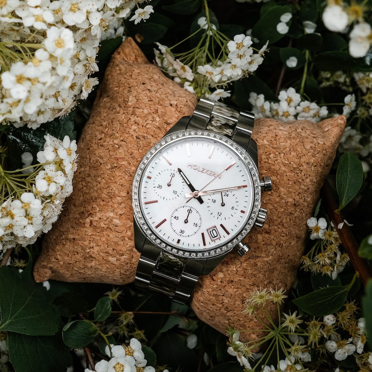 "The Balanced", a stylish wristwatch featuring nacre and silver elements, elegantly displayed among delicate white flowers.