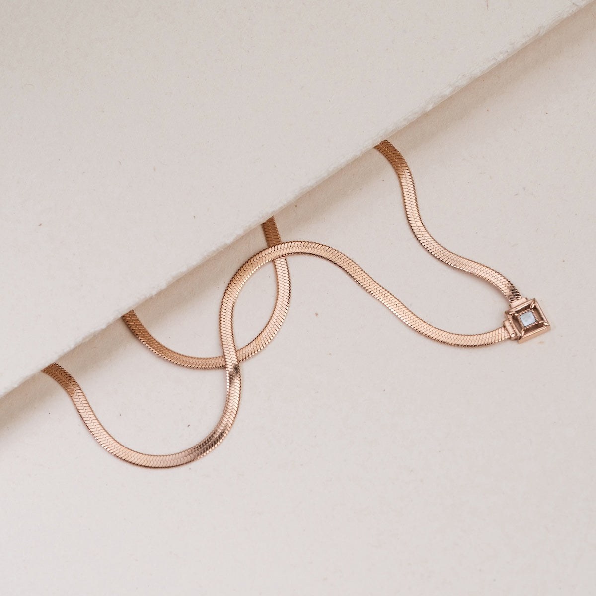 "Awakening Necklace", a rose gold necklace with an elegant nacre accent, lying on a soft white surface.